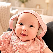 Elsa is registered to the contest to win money with this photo: baby, infant, headphones, pink, smile, cute, face, portrait, child, indoors, bib, soft_lighting, happy, young_child, apparel, sitting, technology, headwear, cozy, blurred_background