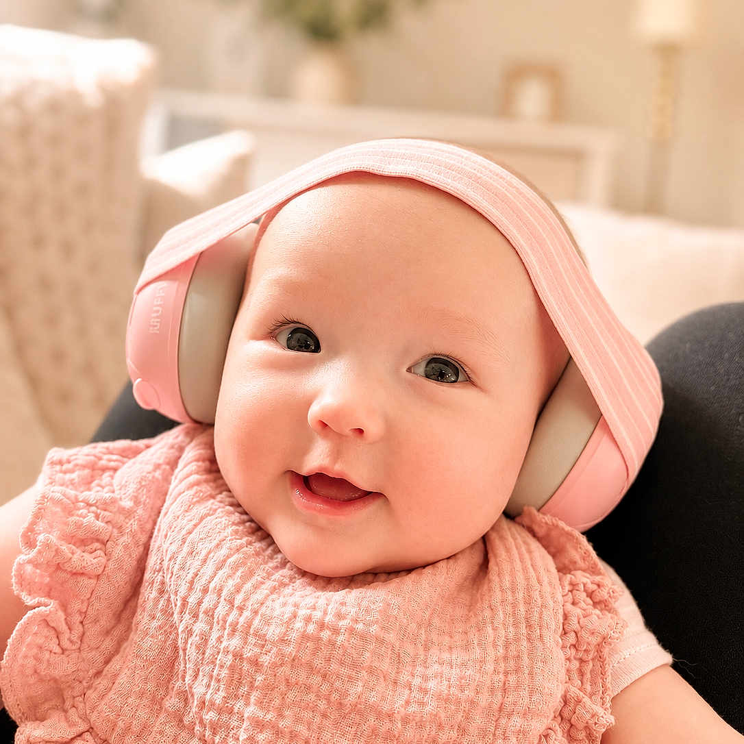 Elsa is registered to the contest to win money with this photo: baby, infant, headphones, pink, smile, cute, face, portrait, child, indoors, bib, soft_lighting, happy, young_child, apparel, sitting, technology, headwear, cozy, blurred_background