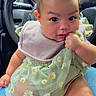 baby, child, infant, sitting, car_interior, steering_wheel, green_dress, daisies, bib, curious, hand, legs, cute, rosy_cheeks, person, seat, lap, clothing, indoor, portrait