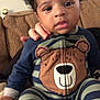 baby, child, pajamas, striped_clothing, bear_design, couch, hand, indoor, portrait, curly_hair, person, seated, comfort, casual, cute, young_child, home, expression, face, support