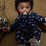 baby, pacifier, pajamas, couch, infant, child, sitting, indoor, curly_hair, footwear, clothing, pattern, face, person, comfortable, relaxing, young_child, home, cute, portrait