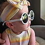 Aaliyah is registered to the contest to win money with this photo: baby, child, sunglasses, headband, striped_clothing, pastel_colors, indoor, portrait, fashion, cute, soft_light, closeup, person, infant, accessory, arm, face, profile, comfortable, hand