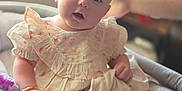 Aaliyah is registered to the contest to win money with this photo: baby, child, plush_toy, dress, cushion, indoor, window, human_arm, infant, person, soft_toy, seated, cute, curious, bracelet, light, home, closeup, skin, furniture