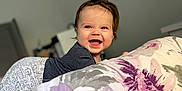 Tyson is registered to the contest to win money with this photo: baby, bed, bedroom, blanket, clothing, cushion, face, furniture, happy, head, homedecor, indoors, laughing, person, photography, portrait, purple, quilt, room, smile