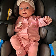 Mabel is registered to the contest to win money with this photo: baby, infant, car_seat, pink_clothing, headband, bow, straps, seat, child, cute, drool, portrait, indoors, child_seat, person, young_child, apparel, seatbelt, comfort, expression