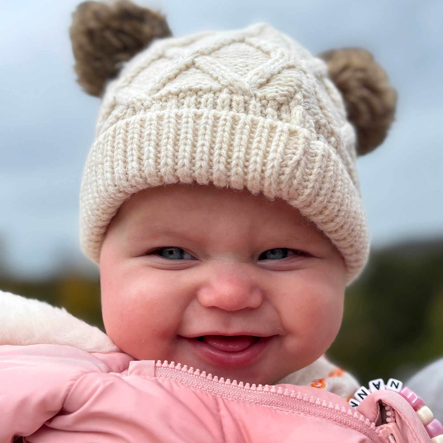 Mabel is registered to the contest to win money with this photo: baby, blue_eyes, cheeks, child, closeup, cold_weather, cute, face, hand, happy, hat, knit_hat, outdoor, person, pink_jacket, pom_poms, portrait, smiling, winter_clothing, zipped_jacket