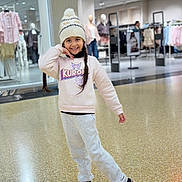 Avneet Kaur joined the competition — help win amazing prizes! child, girl, smiling, portrait, fashion, clothing_store, shopping_mall, beanie, pom_pom, sweatshirt, joggers, sandals, braids, standing, posing, indoors, retail, mannequins, clothing_racks, happy