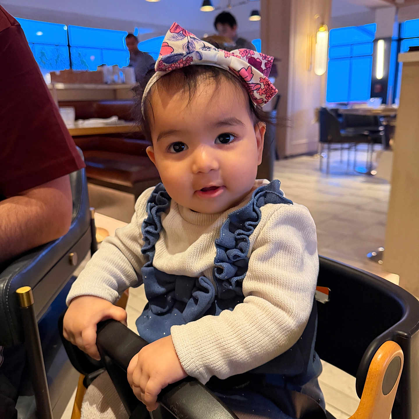 Avleen joined the competition — help win amazing prizes! baby, child, toddler, portrait, restaurant, high_chair, bow, floral, outfit, ruffles, smiling, wide_eyed, sitting, indoor, dining_area, booth, warm_lighting, family, person, photography