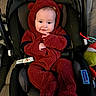 baby, child, car_seat, onesie, red_clothing, plush, cute, indoor, toy, seatbelt, smiling, face, infant, childcare, cozy, portrait, person, warm_clothing, hand, head