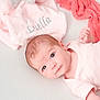 baby, infant, plush_toy, elephant_toy, blanket, pink_blanket, embroidered_text, coral_cloth, soft_texture, white_background, laying_down, cute, newborn, child, face, skin, clothing, portrait, resting, looking