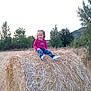 Maëlys a rejoint le concours — aidez-le/la à gagner de superbes lots ! blue_jeans, casual_clothing, child, daylight, field, footwear, girl, grass, happy, hay_bale, hill, nature, outdoor, pink_shirt, playful, rural, sitting, smile, trees, young_child