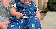 Lainey is registered to the contest to win money with this photo: baby, child, red_bow, headband, denim, floral, outdoor, building, sidewalk, adult, person, shoe, sneakers, cute, tongue, holding, casual, greenery, portrait, smile