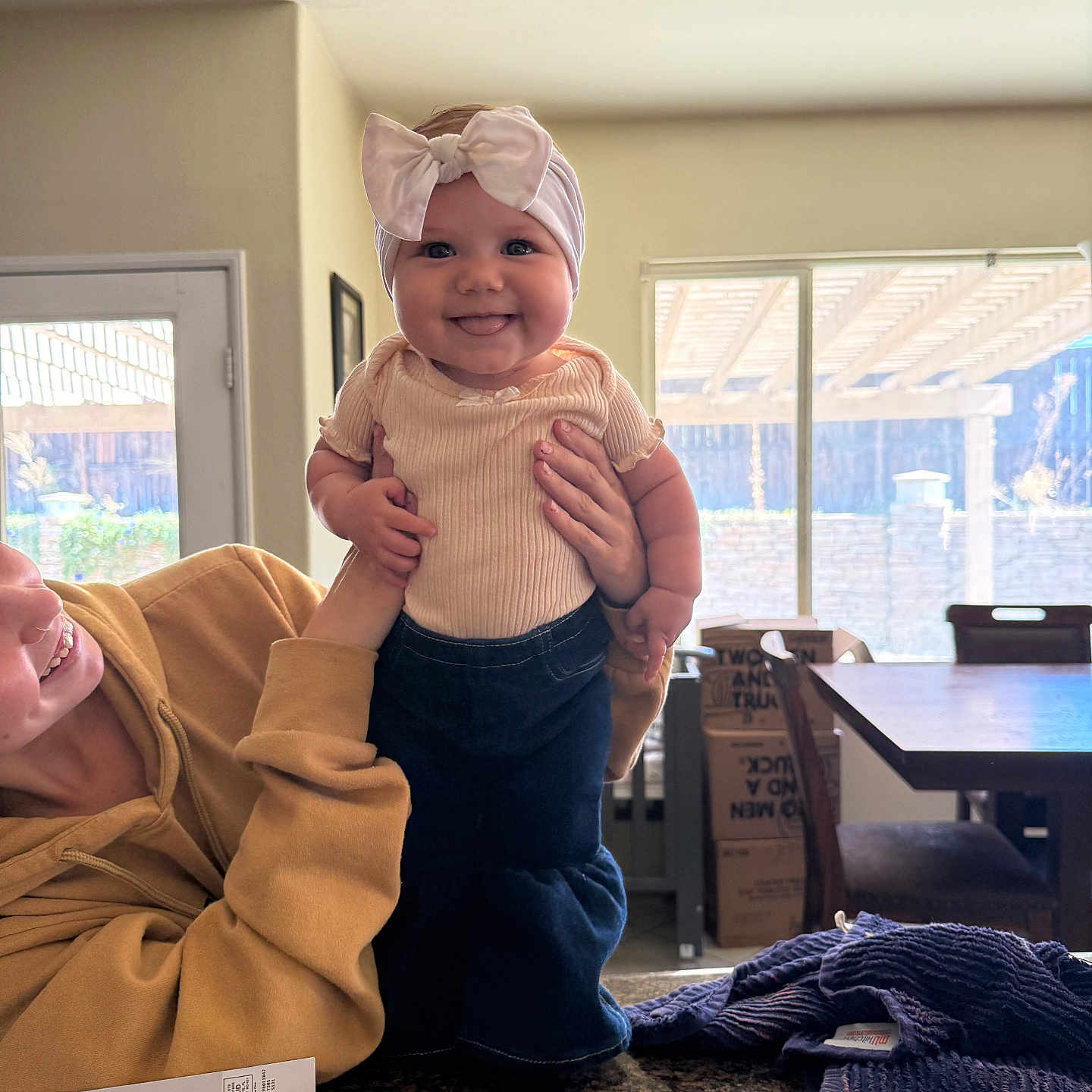 Lainey joined the competition — help win amazing prizes! baby, child, headband, bow, smile, person, indoor, window, table, chair, sweater, denim, hands, face, light, home, kitchen, happy, people, holding