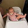 Lainey is registered to the contest to win money with this photo: baby, high_chair, pacifier, pink_onesie, blue_eyes, baby_leg, baby_arm, indoor, wall, dog, floor_tile, baby_face, baby_hair, baby_clothing, child, pet, curious, infant, furniture, home