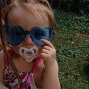 Tessa is registered to the contest to win money with this photo: toddler, child, sunglasses, pacifier, outdoor, grass, summer, hair_ties, swimsuit, minnie_mouse, hand, pointing, cute, baby, person, playful, colorful, fun, portrait, sunny