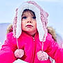 child, toddler, winter_clothing, pink_jacket, fluffy_hat, pom_poms, blue_eyes, snow, outdoor, cold_weather, winter, portrait, face, curious, young_child, warm_clothing, close_up, person, hat, cute