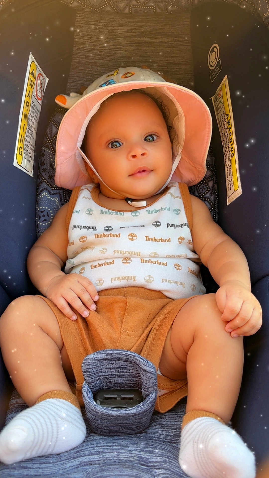 Jasai is registered to the contest to win money with this photo: baby, infant, car_seat, hat, clothing, socks, child, cute, portrait, smiling, indoors, seatbelt, warning_label, timberland, skin, hand, footwear, baby_clothes, headwear, child_safety