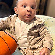 Jasai is registered to the contest to win money with this photo: baby, child, basketball, clothing, jacket, pants, person, indoor, sitting, toy, face, hand, necklace, earrings, expression, cute, infant, soft_lighting, closeup, portrait