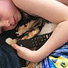 child, cat, calico_cat, cuddling, sleeping, indoors, bedroom, blanket, remote_control, couch, portrait, face, arms, brown_hair, cozy, relaxed, pet, domestic_animal, colorful_blanket, family