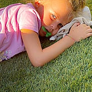 Jodie participe au concours pour gagner de l'argent avec cette photo : child, grass, pacifier, pink_shirt, sunlight, outdoor, laying_down, blonde_hair, hair_tie, hand, face, earrings, shadow, fabric, relaxing, nature, daylight, portrait, casual, youth
