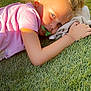 child, grass, pacifier, pink_shirt, sunlight, outdoor, laying_down, blonde_hair, hair_tie, hand, face, earrings, shadow, fabric, relaxing, nature, daylight, portrait, casual, youth