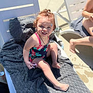 Scarlett is registered to the contest to win money with this photo: accessory, barefoot, child, hair_tied, happy, lounge_chair, outdoor, person, playful, poolside, relaxation, skin, smiling, summer, sunglasses, sunlight, sunny, swimsuit, toddler, towel