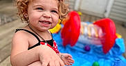 Scarlett joined the competition — help win amazing prizes! background, blur, child, curly_hair, daylight, deck, hand, happy, inflatable_pool, leg, outdoor, person, playing, red_bow, skin, smile, summer, swimsuit, toddler, toys