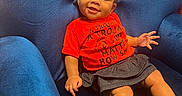Jalaia is registered to the contest to win money with this photo: baby, child, smiling, blue_chair, red_shirt, skirt, sitting, happy, cute, indoors, plush_furniture, person, portrait, small_child, cozy, casual_clothing, barefoot, infant, expression, comfort