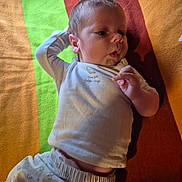 Mickael participe au concours pour gagner de l'argent avec cette photo : baby, blanket, child, clothing, colorful, curious, expression, face, hand, indoor, infant, lying_down, newborn, patterned, portrait, resting, soft_light, toddler, white_outfit, young_child