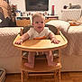 baby, high_chair, tongue_out, wooden_furniture, living_room, television, photoframes, cushion, blanket, floor, flooring, person, child, smile, happy, indoors, wood, seat, clothing, home