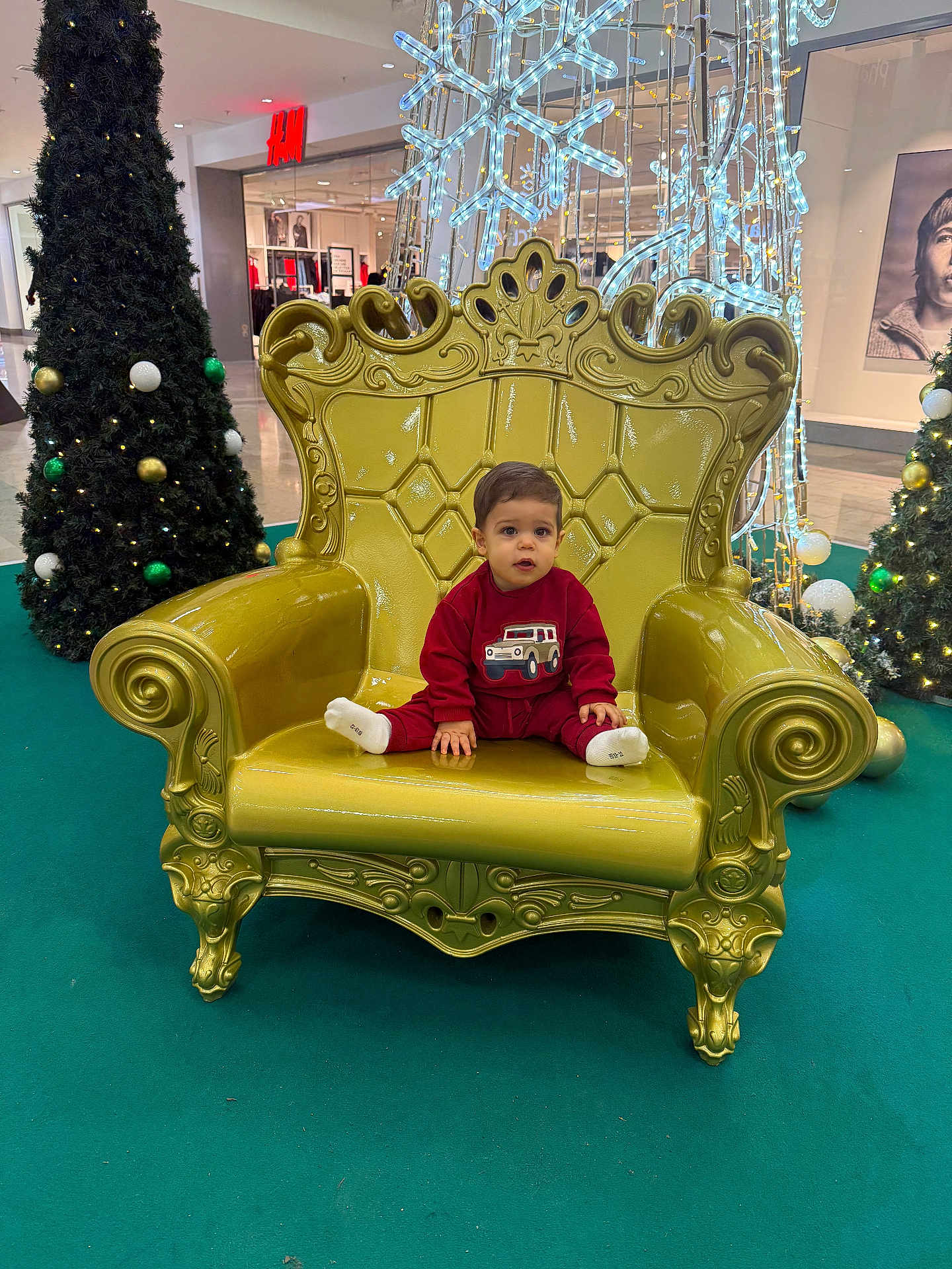 Mattéo Cristiano participe au concours pour gagner de l'argent avec cette photo : toddler, child, red_clothing, golden_chair, ornate_chair, christmas_trees, holiday_lights, mall, indoor, festive, decorations, carpet, face, portrait, seated, toy_car_image, expression, holiday_season, winter, shopping