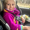 Haley is registered to the contest to win money with this photo: child, car_seat, seatbelt, smile, purple_sweater, colorful_clothing, car_interior, window, forest, forest_view, happy, young_child, person, casual_wear, portrait, indoors, seat, safety, daylight, cute