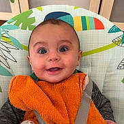 Alexandro participe au concours pour gagner de l'argent avec cette photo : baby, infant, smile, bib, harness, buckle, wide_eyes, chubby_cheeks, baby_bouncer, high_chair, orange_towel, patterned_backdrop, indoor, hand, sleeve, clothing, seat, teething_toy, wooden_cabinet, portrait