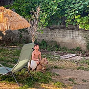 Sayane participe au concours pour gagner de l'argent avec cette photo : boy, dog, grass, outdoor, backyard, sunny, greenery, lounge_chair, umbrella, tree, fence, smiling, shirtless, pet, summer, nature, relaxation, playing, child, animal