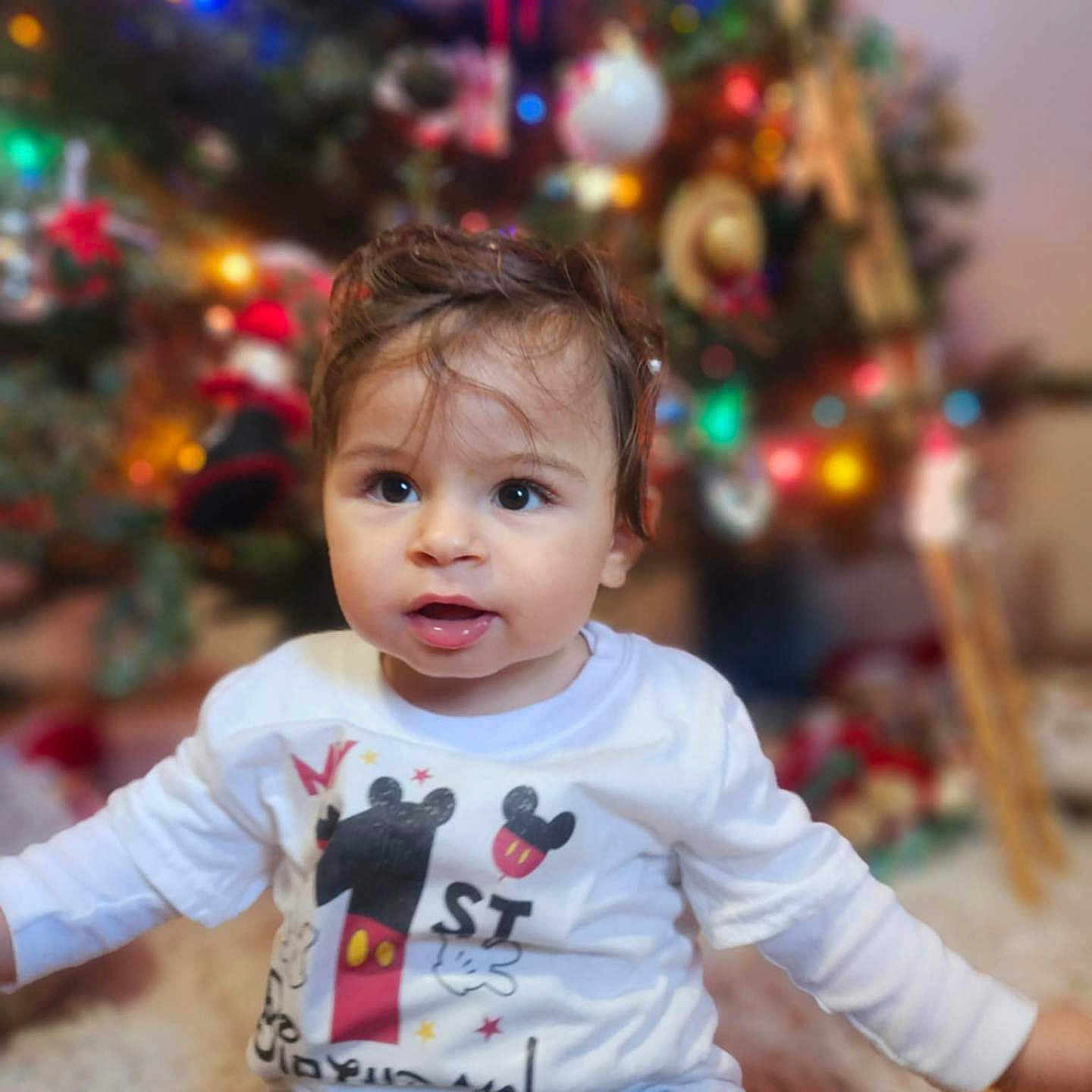 Zaid joined the competition — help win amazing prizes! celebration, child, christmas_tree, cute, decorations, expression, face, festive, floor, holiday, holiday_spirit, home, indoor, jeans, lights, mickey_mouse, shirt, sitting, toddler, young_child