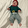 baby, child, infant, smiling, happy, lying_down, bed, blanket, striped_pants, costume, elf, hat, feet, cute, clothing, indoors, person, face, headwear, playful