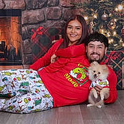 Tiger is registered to the contest to win money with this photo: couple, dog, christmas_tree, fireplace, holiday, pajamas, smiling, gift_box, floor, decorations, festive, indoor, happy, portrait, warmth, celebration, seasonal, togetherness, cute, pet