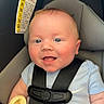 baby, infant, child, smiling, happy, portrait, car_seat, safety_harness, pacifier, pacifier_chain, blue_shirt, seated, indoors, vehicle, close_up, face, eyes, cheeks, carseat_warning_label, safe_travel