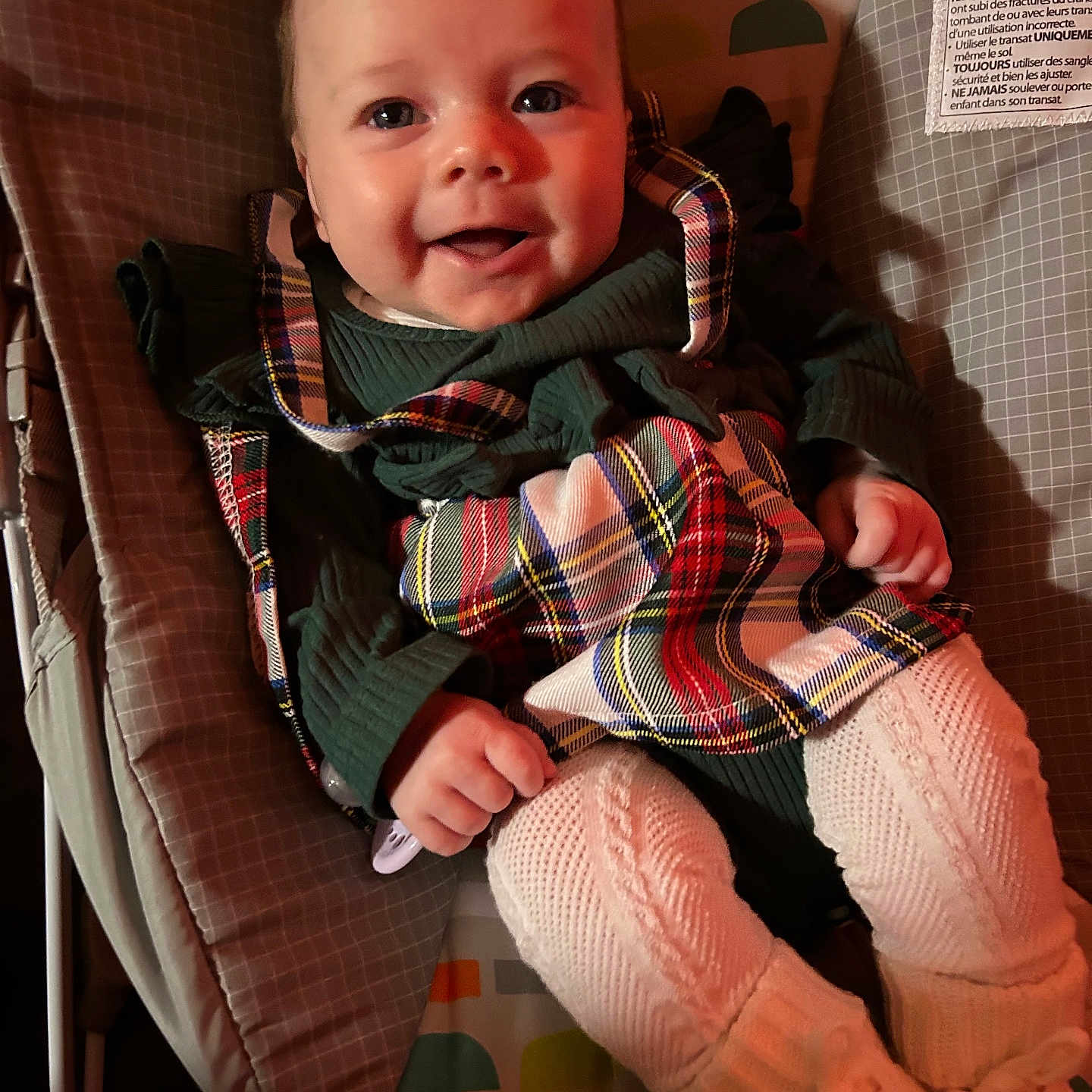 Kylah joined the competition — help win amazing prizes! baby, baby_rocker, child, clothing, cushion, cute, face, footwear, hand, happy, indoor, infant, knitted_tights, person, plaid, portrait, seated, smiling, toddler, warm_lighting