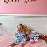 Scarlett joined the competition — help win amazing prizes! baby, child, smiling, blue_outfit, stuffed_animals, bunny, bed, pink_wall, wooden_letters, nursery, plush_toys, happy, sitting, curly_hair, headband, pink_bedspread, indoor, decor, cute, person