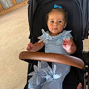 Scarlett is registered to the contest to win money with this photo: toddler, child, stroller, blue_bow, blue_outfit, fabric_flowers, curly_hair, indoor, wooden_wall, metal_panels, barefoot, cute, sitting, baby, portrait, casual, light, daylight, expression, small_hands