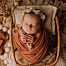 newborn, baby, swaddled, sleeping, wicker_basket, knitted_toy, bunny, headband, floral, cozy, rust_color, wooden_floor, decorative_pillow, soft_texture, peaceful, portrait, indoors, baby_photography, cute, infant