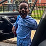 child, boy, blue_clothing, nike, tracksuit, backpack, car_door, open_car_door, urban, brick_building, fence, excited, happy, standing, outdoor, smiling, person, daylight, road, sidewalk