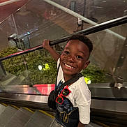 Joash is registered to the contest to win money with this photo: child, boy, smile, escalator, urban, night, railing, white_shirt, sunglasses, crocs, happy, portrait, casual_clothing, glass, reflection, background, person, standing, looking_up, handrail