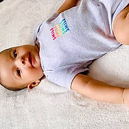 Fateh is registered to the contest to win money with this photo: baby, child, infant, smile, onesie, clothing, skin, face, arm, hand, blanket, soft, lying_down, cute, young, portrait, indoor, peaceful, relaxed, comfort
