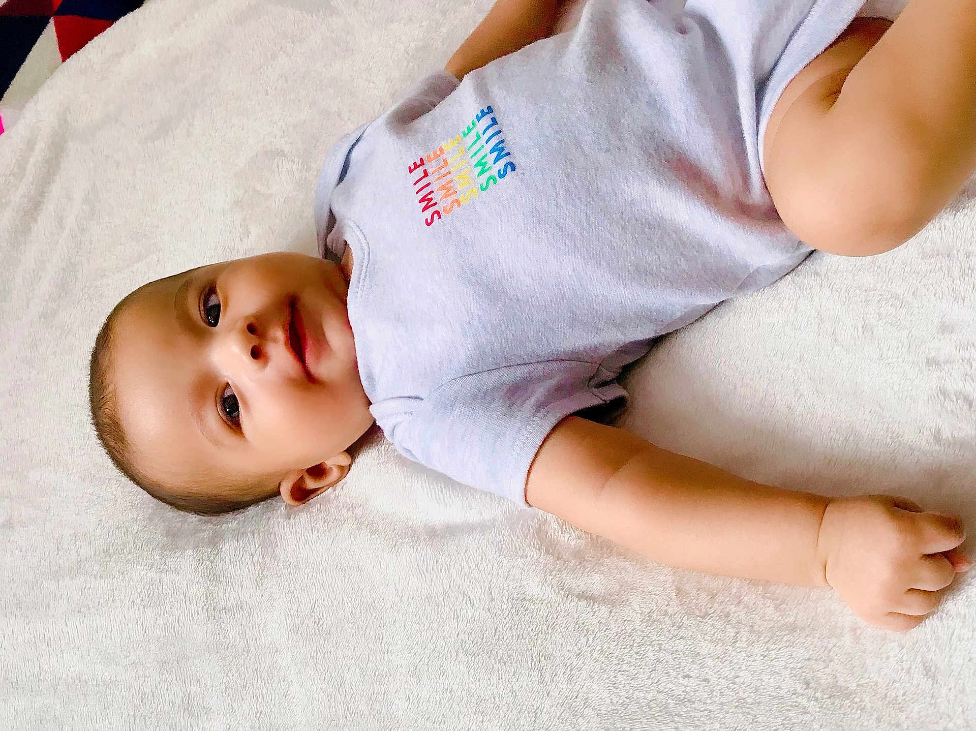 Fateh is registered to the contest to win money with this photo: baby, child, infant, smile, onesie, clothing, skin, face, arm, hand, blanket, soft, lying_down, cute, young, portrait, indoor, peaceful, relaxed, comfort