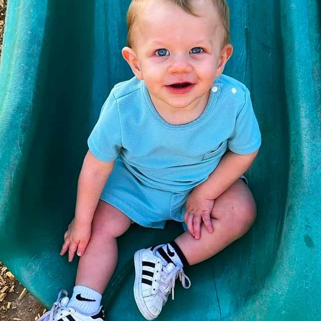 Greggie is registered to the contest to win money with this photo: baby, clothing, face, footwear, happy, head, jeans, outdoorplayarea, outdoors, pants, person, photography, playarea, portrait, shoe, sitting, slide, sliding, sneaker, toy