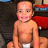 Miloh is registered to the contest to win money with this photo: toddler, child, smiling, lipstick_marks, couch, curly_hair, diaper, indoor, happy, face, arms, legs, skin, red_marks, toy_box, cushions, home, person, sitting, playful