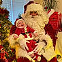 baby, child, santa_claus, christmas_tree, holiday, festive, decorations, indoor, smile, red_clothing, white_beard, gloves, hat, potted_plant, mailbox, toy_elf, lights, happy, person, celebration