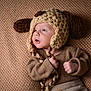baby, infant, knitted_hat, dog_ears, brown_clothing, textured_blanket, cute, portrait, indoor, soft_lighting, hand, face, expression, newborn, cozy, warm_colors, looking_up, fingers, headwear, child
